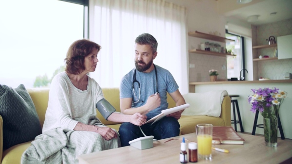 Health visitor and a senior woman during home visit, checking blood pressure. Slow motion.