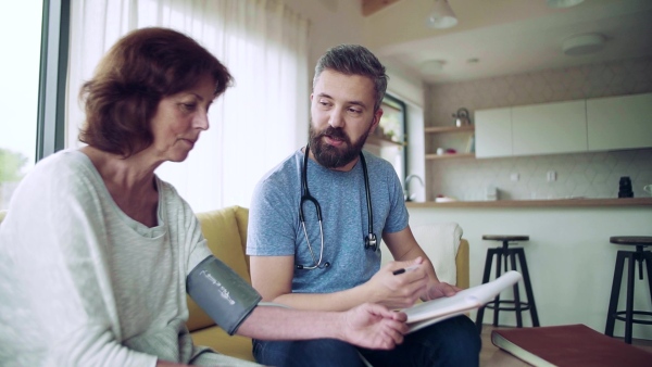 Health visitor and a senior woman during home visit, checking blood pressure. Slow motion.