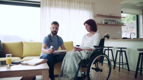 Health visitor and a senior woman in wheelchair during home visit, talking about taking medication. Slow motion.