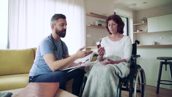 Health visitor and a senior woman in wheelchair during home visit, talking about taking medication. Slow motion.