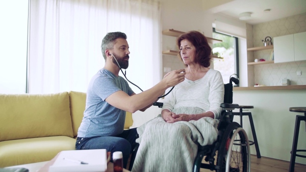 Health visitor and a senior woman during home visit, checking of blood pressure. Slow motion.