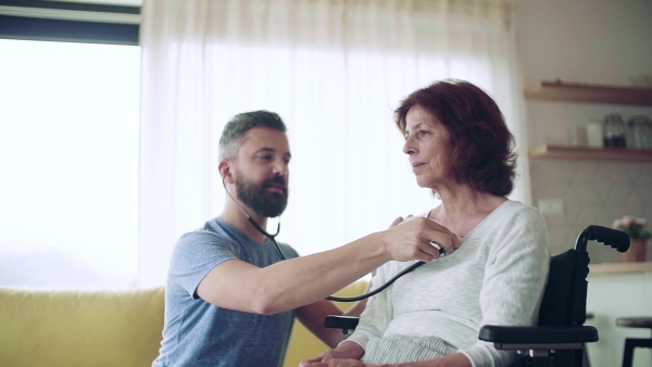 Health visitor examining a senior woman during home visit with stethoscope. Slow motion.