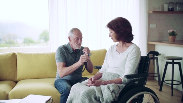 Health visitor examining a senior woman in wheelchair with stethoscope during home visit. Slow motion.