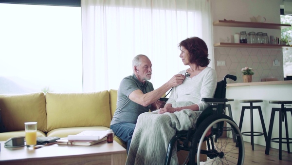 Health visitor examining a senior woman in wheelchair with stethoscope during home visit. Slow motion.