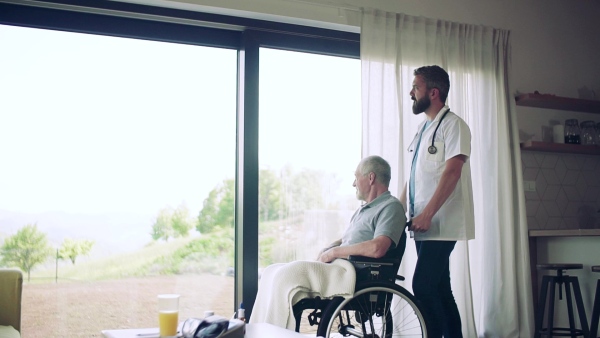 A health visitor and a senior man in wheelchair during home visit, talking. Slow motion.