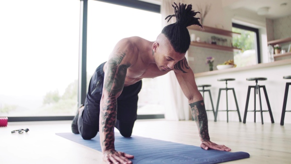 A mixed race young man with tattoo doing exercise indoors at home, a body workout.