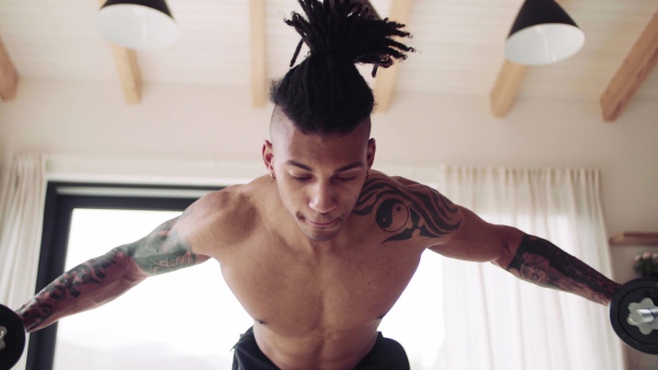 A mixed race young man doing exercise with dumbbells indoors at home, a body workout.