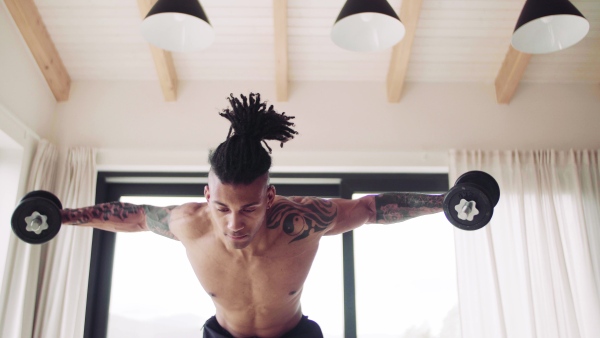 A mixed race young man doing exercise with dumbbells indoors at home, a body workout.