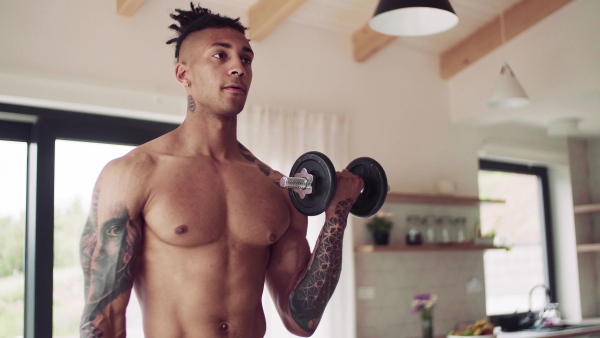 A mixed race young man doing exercise with dumbbells indoors at home, a body workout.