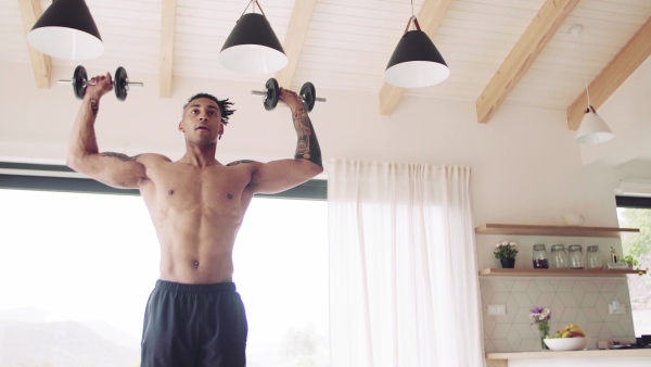 A mixed race young man doing exercise with dumbbells indoors at home, a body workout.