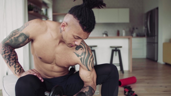 A mixed race young man doing exercise with dumbbells indoors at home, a body workout.