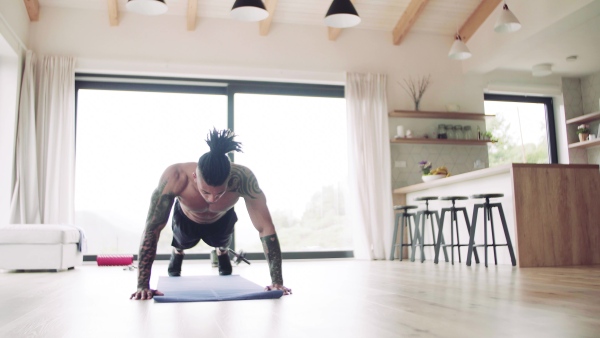 A mixed race young man with tattoo doing exercise indoors at home, a body workout.