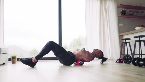 A mixed race young man with foam roller doing exercise indoors at home, a body workout.