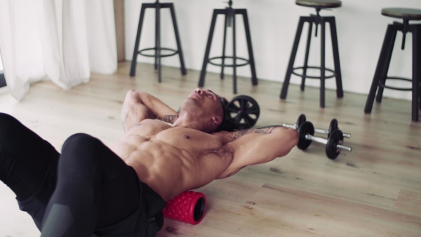 A mixed race young man with foam roller doing exercise indoors at home, a body workout.