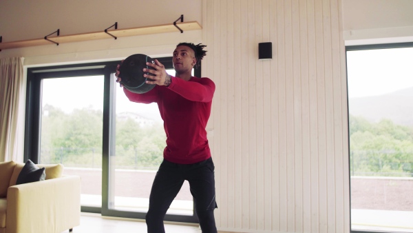 A mixed race young man doing exercise with heavy ball indoors at home, a body workout.