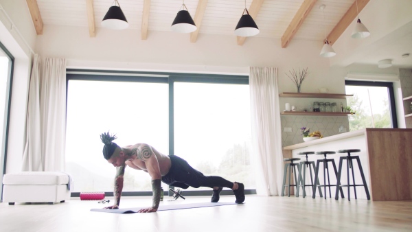 A mixed race young man with tattoo doing exercise indoors at home, a body workout.