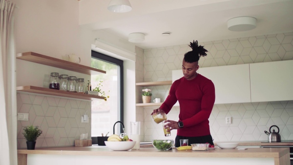 An active mixed race young sporty man indoors at home, making smoothie.