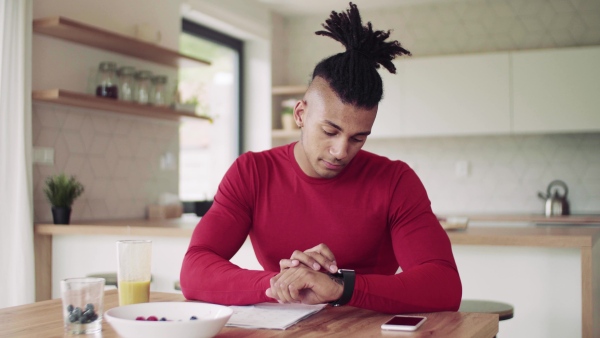 A mixed race young sporty man with smartwatch indoors at home, drinking juice.