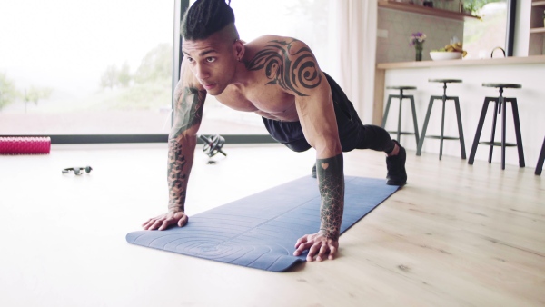 A mixed race young man with tattoo doing exercise indoors at home, a body workout.