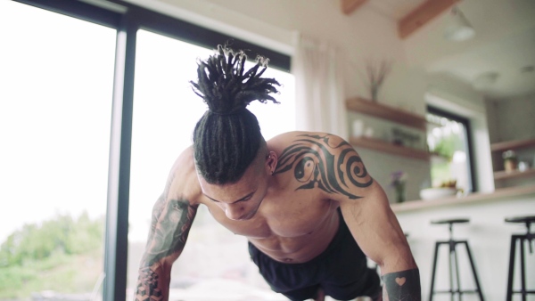 A mixed race young man with tattoo doing exercise indoors at home, a body workout. Slow motion.