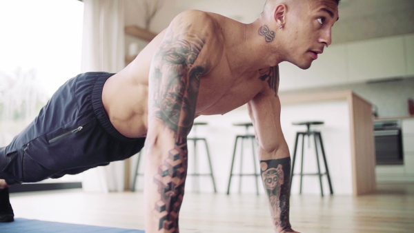 A mixed race young man with tattoo doing exercise indoors at home, a body workout. Slow motion.