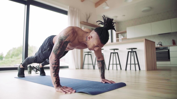 A mixed race young man with tattoo doing exercise indoors at home, a body workout. Slow motion.