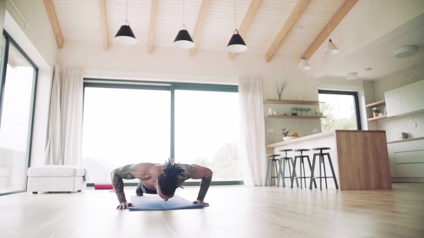 A mixed race young man with tattoo doing exercise indoors at home, a body workout. Slow motion.