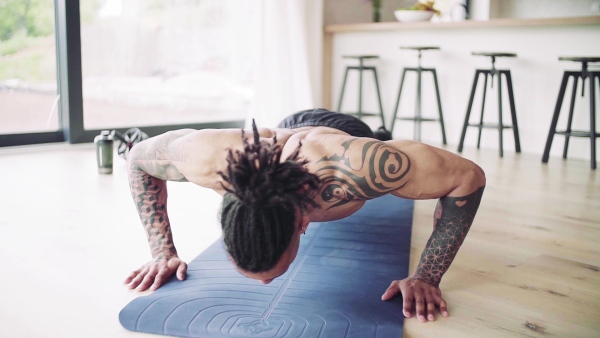 A mixed race young man with tattoo doing exercise indoors at home, a body workout. Slow motion.