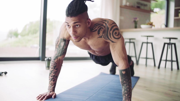 A mixed race young man with tattoo doing exercise indoors at home, a body workout. Slow motion.