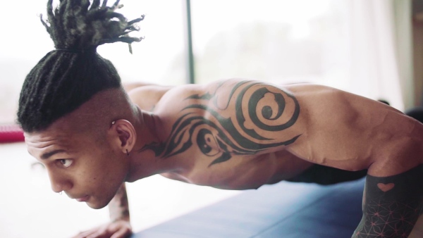 A mixed race young man with tattoo doing exercise indoors at home, a body workout. Slow motion.