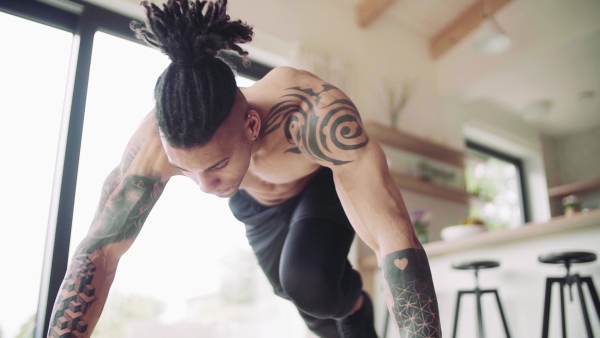 A mixed race young man with tattoo doing exercise indoors at home, a body workout. Slow motion.