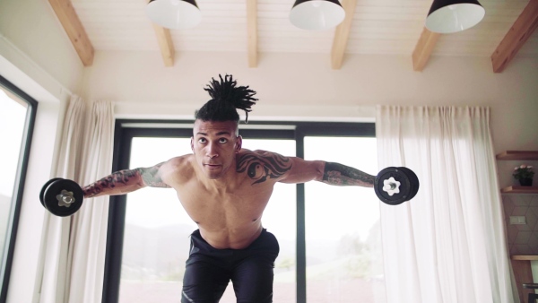 A mixed race young man doing exercise with dumbbells indoors at home, a body workout. Slow motion.