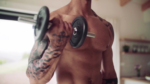 Midsection of young man with dumbbell doing exercise indoors at home, a body workout. Slow motion.