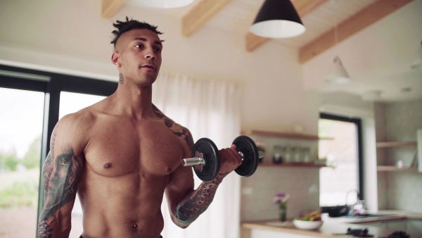 A mixed race young man doing exercise with dumbbells indoors at home, a body workout. Slow motion.