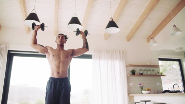 A mixed race young man doing exercise with dumbbells indoors at home, a body workout. Slow motion.