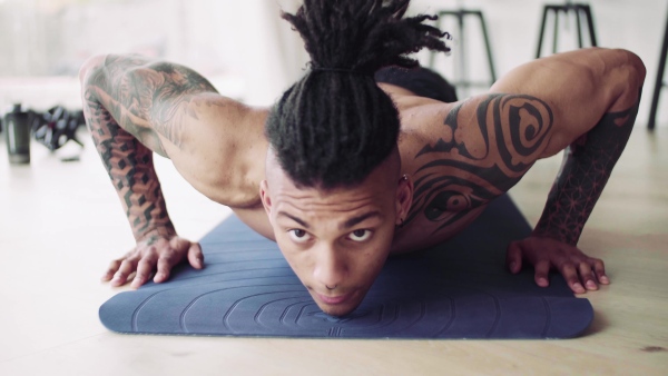 A mixed race young man with tattoo doing exercise indoors at home, a body workout.