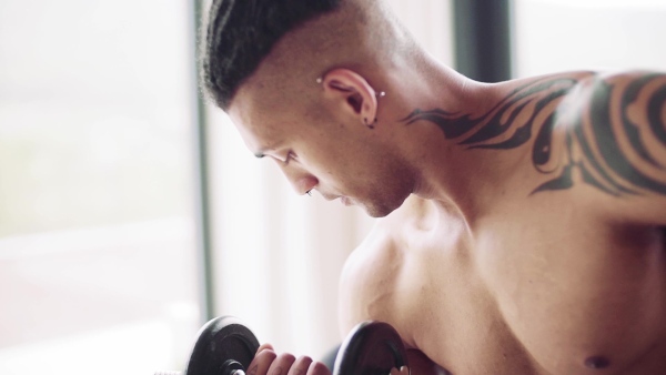 A mixed race young man doing exercise with dumbbells indoors at home, a body workout. Slow motion.