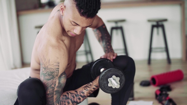 A mixed race young man doing exercise with dumbbells indoors at home, a body workout. Slow motion.