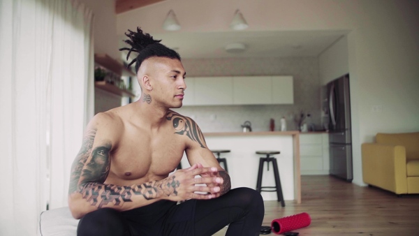 A mixed race young man resting after exercise indoors at home, a body workout. Slow motion.