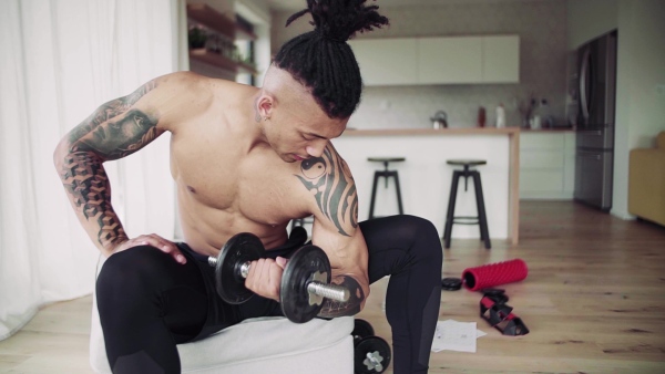 A mixed race young man doing exercise with dumbbells indoors at home, a body workout. Slow motion.