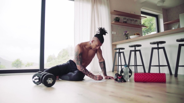 A mixed race young man with tattoo doing exercise indoors at home, a body workout. Slow motion.