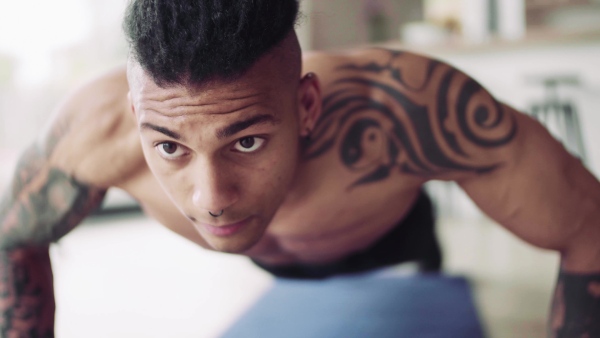 A mixed race young man with tattoo doing exercise indoors at home, a body workout.