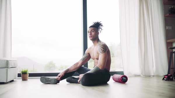 A mixed race young man resting after exercise indoors at home, a body workout. Slow motion.