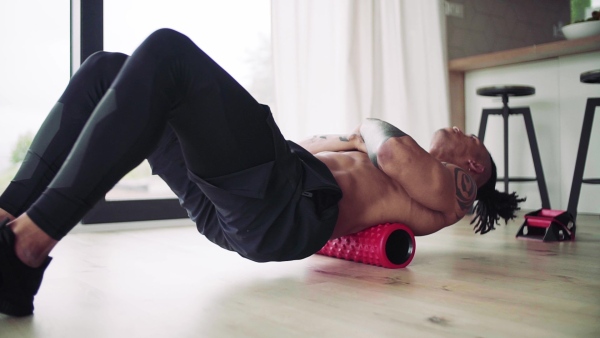 A mixed race young man with foam roller doing exercise indoors at home, a body workout. Slow motion.