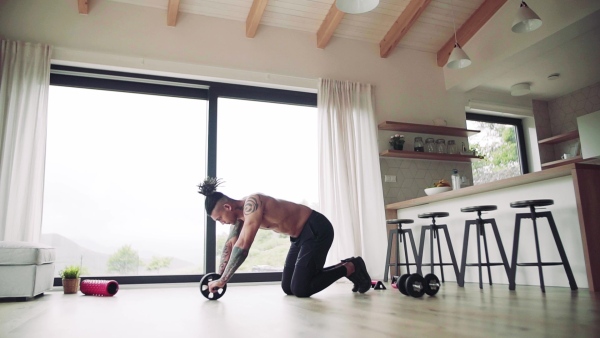 A mixed race young man with tattoo doing exercise indoors at home, a body workout. Slow motion.