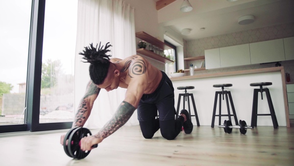 A mixed race young man with tattoo doing exercise indoors at home, a body workout. Slow motion.