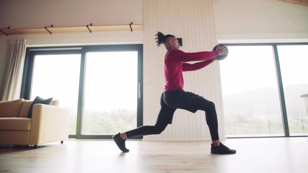 A mixed race young man doing exercise with heavy ball indoors at home, a body workout. Slow motion.