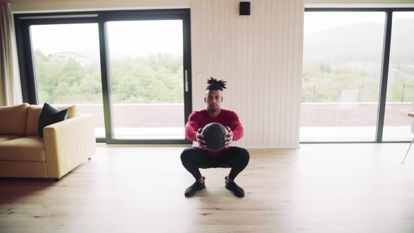 A mixed race young man doing exercise with heavy ball indoors at home, a body workout. Slow motion.