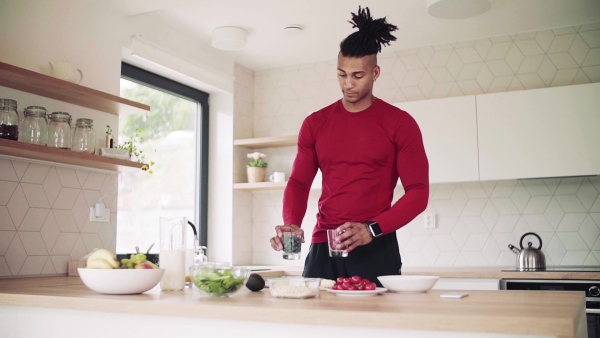 An active mixed race young sporty man indoors at home, preparing healthy food. Slow motion.