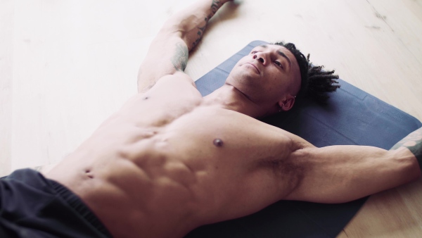 A mixed race young man with tattoo doing exercise indoors at home, a body workout.